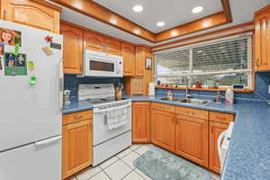 Kitchen with white appliances, dark countertops, a raised ceiling, light tile patterned floors, and recessed lighting