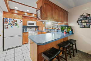 Kitchen featuring a breakfast bar area, white appliances, a peninsula, wood finish cabinetry, and light tile patterned floors