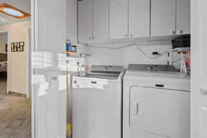 Laundry room featuring light carpet, washer and clothes dryer, cabinet space, and a textured ceiling