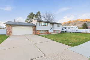Raised ranch with an attached garage, concrete driveway, a mountain view, and brick siding