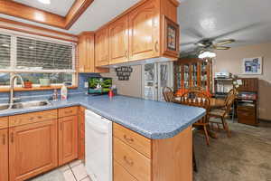 Kitchen with white dishwasher, ceiling fan, a peninsula, and dark countertops