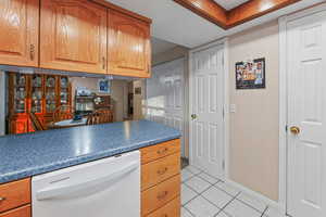 Kitchen featuring dishwasher, light tile patterned floors, dark countertops, and wood finish cabinets