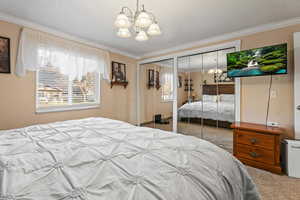 Carpeted bedroom with two closets, a chandelier, ornamental molding, and a textured ceiling