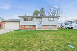 Split foyer home with brick siding, a front lawn, and a chimney