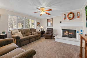 Carpeted living area with crown molding, a textured ceiling, a ceiling fan, and a high end fireplace