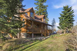 Back of house with covered porch, faux log siding, and a lawn