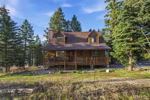 View of front of property with covered porch, a chimney, and view of scattered trees