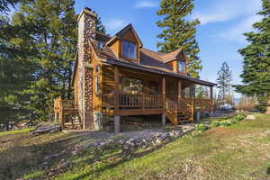 Back of property featuring covered porch, faux log siding, and a chimney