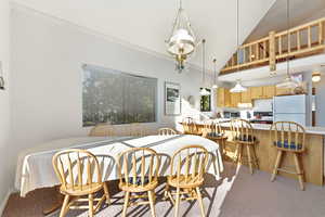 Dining space featuring light colored carpet, lofted ceiling, crown molding, and hanging lights