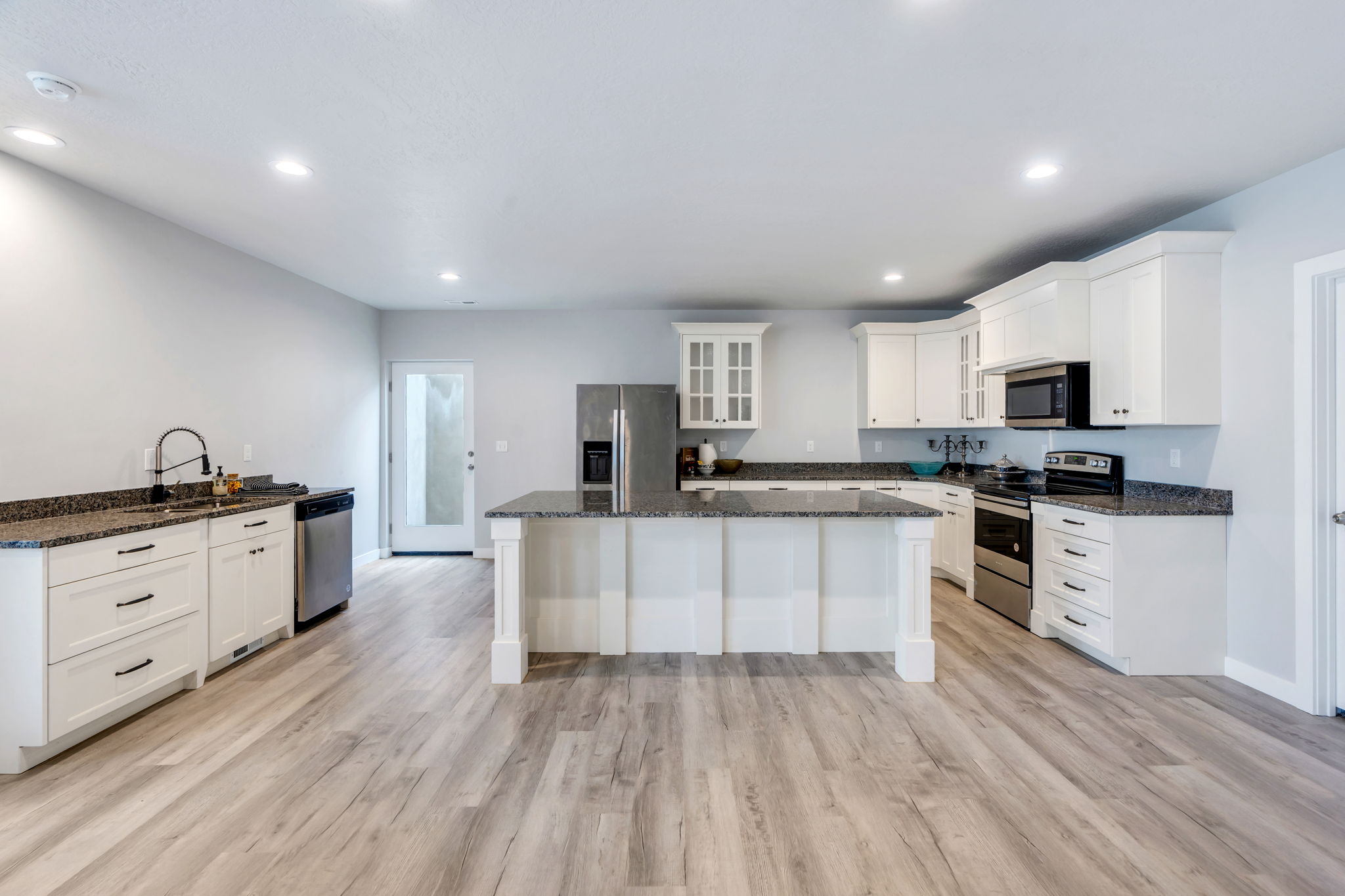 Kitchen with dark stone countertops, stainless steel appliances, white cabinetry, glass fronted cabinets, and recessed lighting