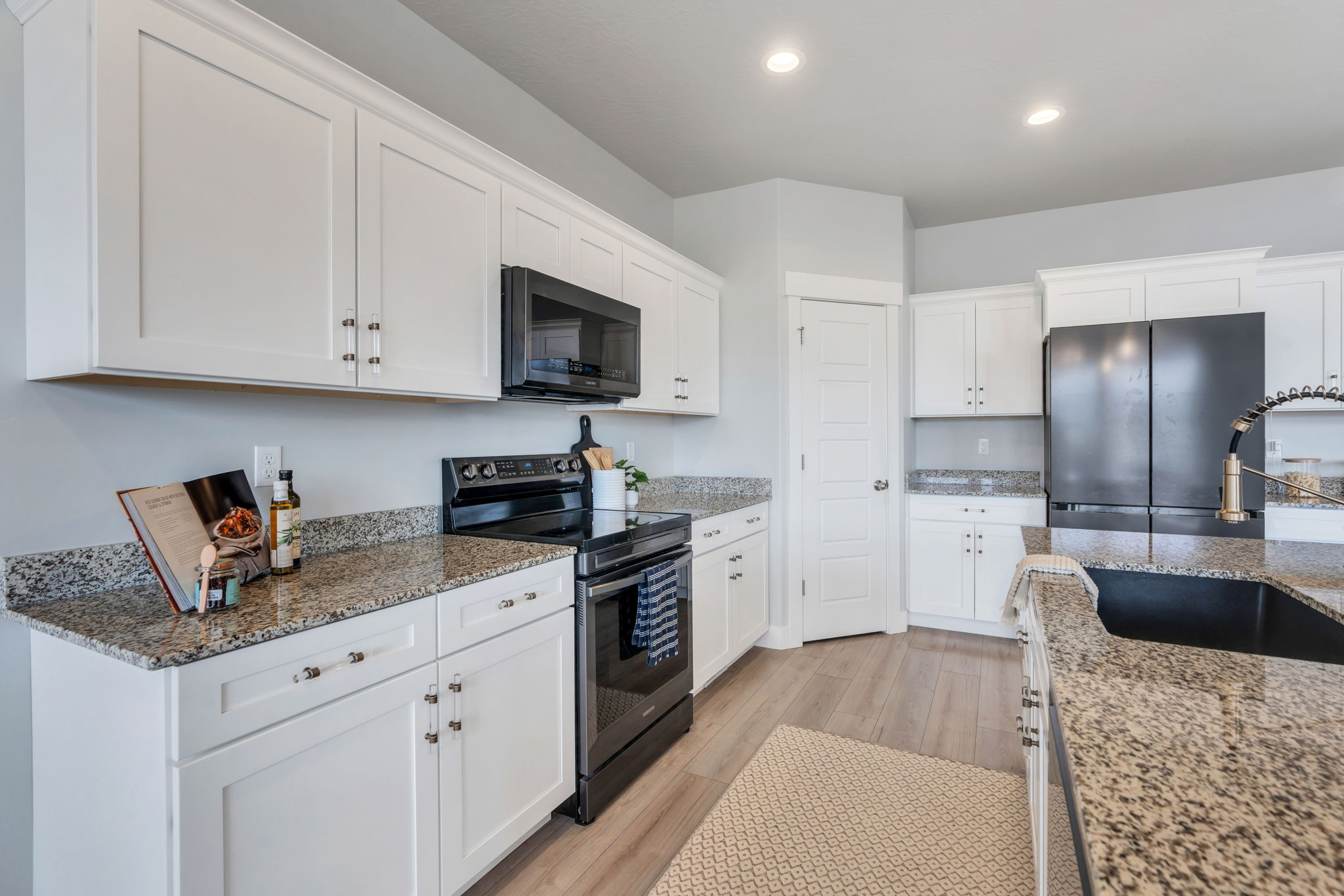 Kitchen featuring electric stove, white cabinets, freestanding refrigerator, black microwave, and light wood-type flooring