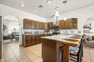 Kitchen with arched walkways, a peninsula, decorative backsplash, a kitchen bar, and pendant lighting