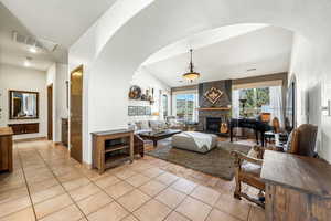 Living area featuring arched walkways, light tile patterned flooring, lofted ceiling, and a fireplace