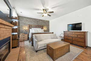 Bedroom featuring brick wall, hardwood / wood-style floors, ceiling fan, and a glass covered fireplace