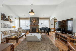Living room featuring a large fireplace, lofted ceiling, light wood-style floors, plenty of natural light, and arched walkways