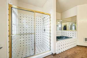 Bathroom featuring a shower stall, wood finished floors, heating unit, and a bath
