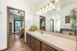 Ensuite bathroom featuring ceiling fan, vanity, and light wood-style floors