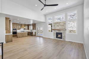 Unfurnished living room with recessed lighting, a high ceiling, a fireplace, light wood-style floors, and a ceiling fan