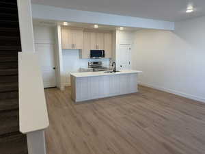 Kitchen with stainless steel appliances, light wood-type flooring, an island with sink, light wood finish cabinets, and recessed lighting