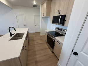 Kitchen featuring light wood finish cabinets, stainless steel appliances, light wood-style floors, and a center island with sink
