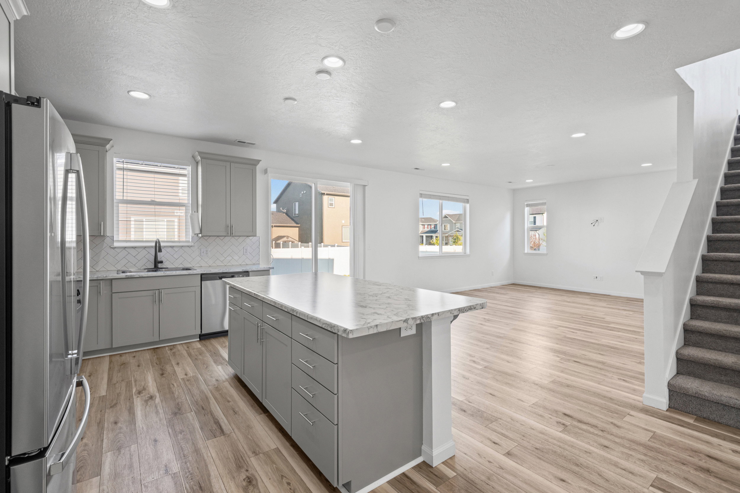 Open-concept living space featuring a kitchen island with stone countertop, stainless steel appliances, wood-finish flooring, recessed lighting, and a carpeted staircase