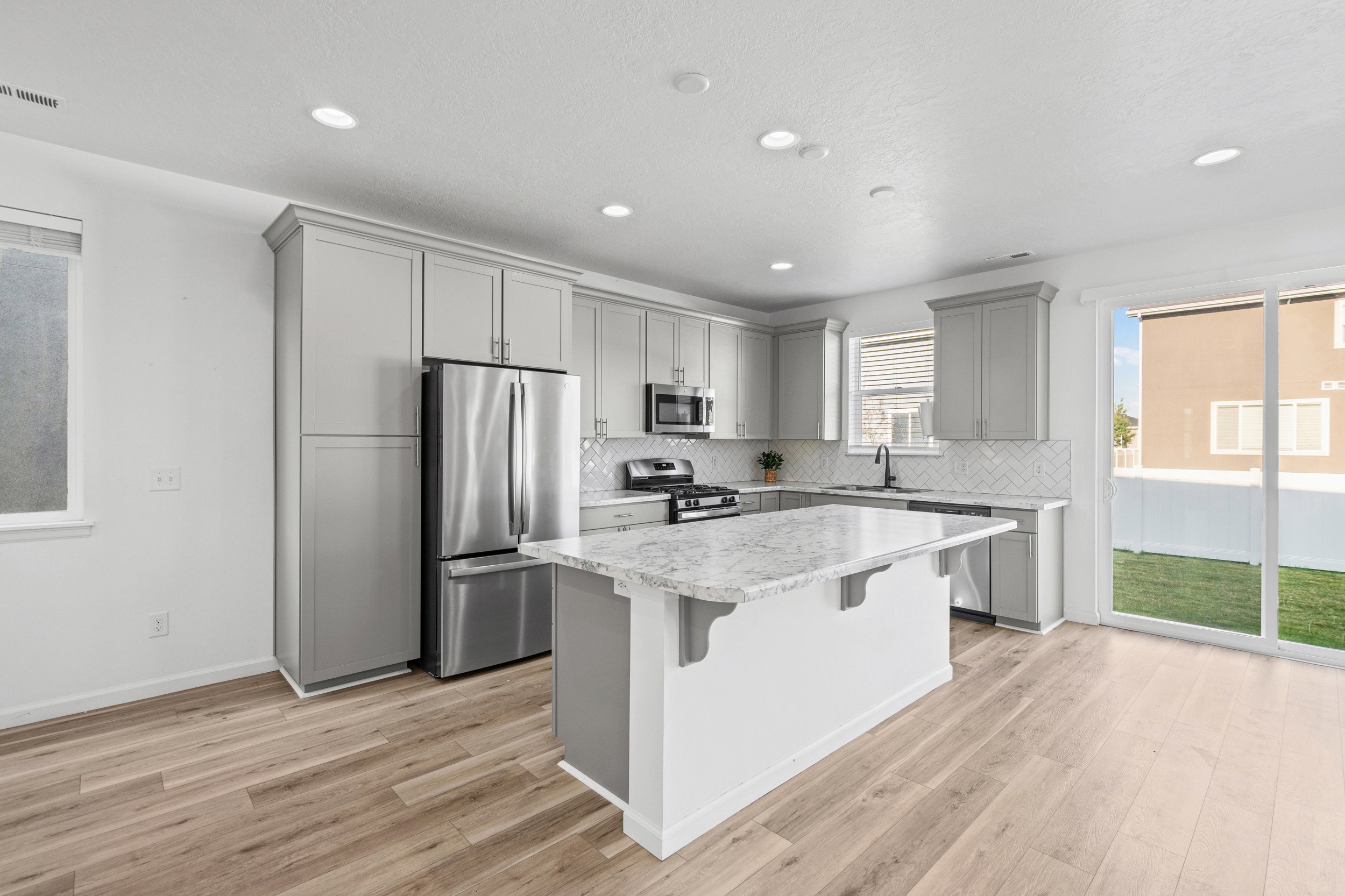 Modern kitchen featuring light gray cabinetry, stainless steel appliances, a center island with a stone countertop, and wood-finish flooring