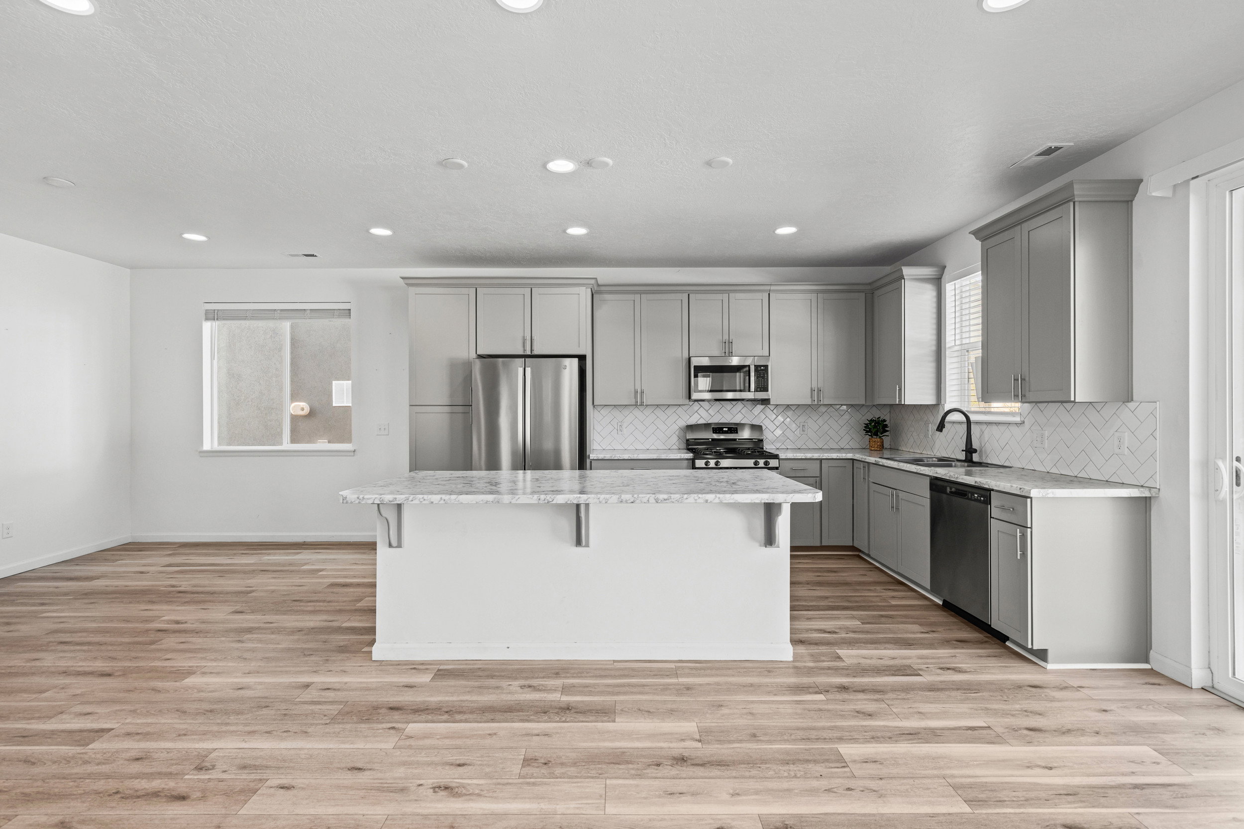 Kitchen featuring a central island with countertop seating, light gray cabinetry, stainless steel appliances, and a white herringbone tile backsplash