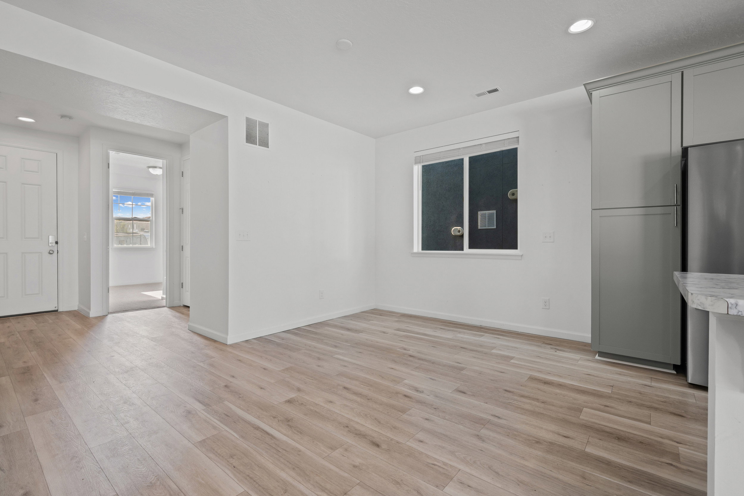 Open-concept living space with light-toned wood-finish flooring, recessed lighting, and white walls