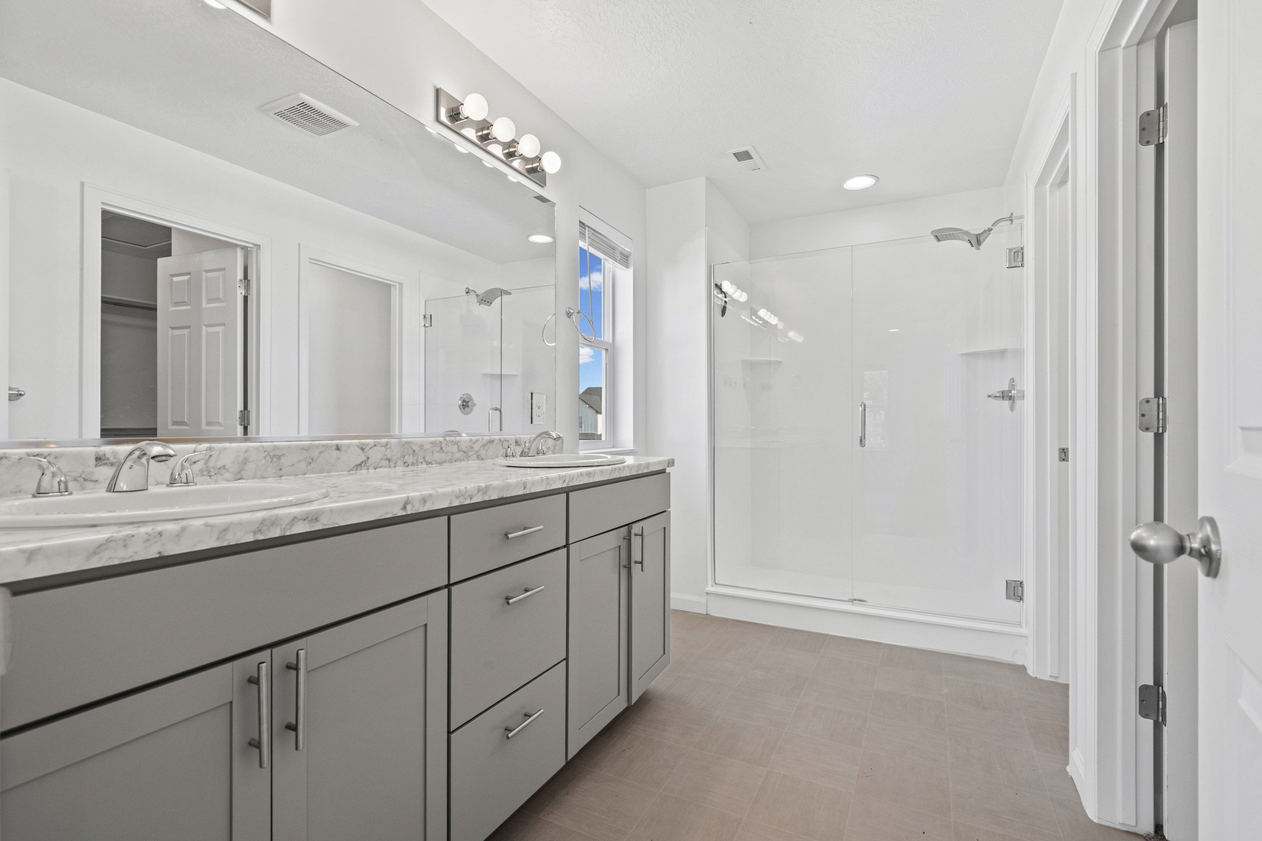 Spacious bathroom featuring a double vanity with grey cabinetry, a patterned countertop, and dual undermount sinks