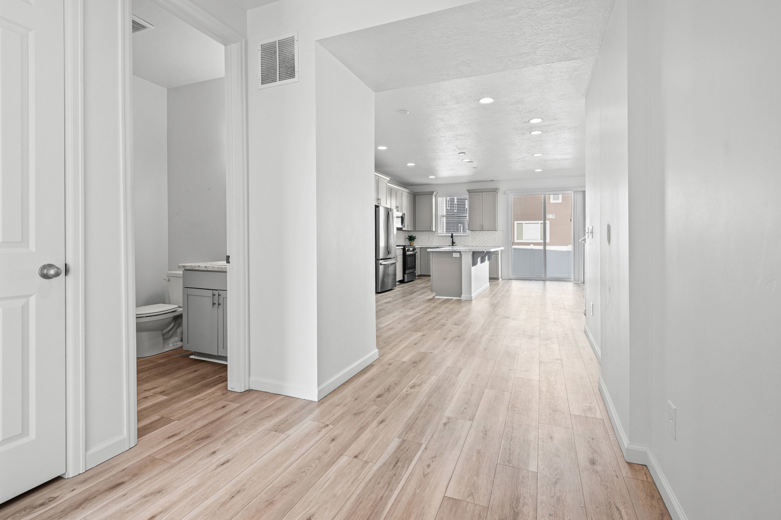 Spacious interior featuring light wood-finish flooring, recessed lighting, a modern kitchen with gray cabinetry, and sliding glass doors
