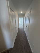 Corridor with baseboards and dark colored carpet