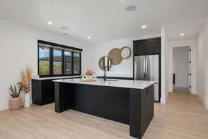 Kitchen featuring an island with sink, freestanding refrigerator, dark cabinets, light wood-style floors, and recessed lighting