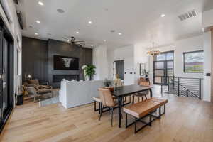 Dining area featuring light wood-style flooring, hanging lights, a large fireplace, ceiling fan, and an accent wall