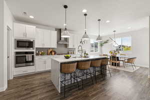 Kitchen featuring waterfall quartz island, gas countertop range, range hood, pendant lighting, soft close drawers and cabinets
