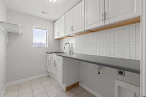Built-out laundry room with counter space, sink, and cabinets