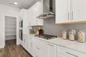 Kitchen featuring waterfall quartz island, gas countertop range, range hood, pendant lighting, soft close drawers and cabinets