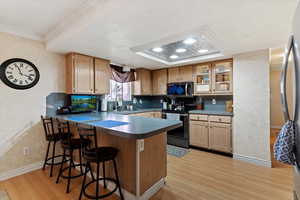 Kitchen with stainless steel appliances, light wood-style flooring, a breakfast bar area, a peninsula, and glass fronted cabinets