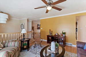 Living room with light wood finished floors, a textured ceiling, crown molding, and a ceiling fan