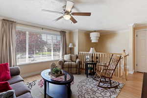 Living room with light wood-type flooring, a ceiling fan, a textured ceiling, and ornamental molding