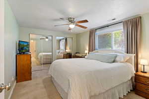 Bedroom with light carpet, two closets, ceiling fan, and a textured ceiling