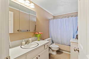 Full bath featuring vanity, crown molding, shower / tub combo, a textured ceiling, and light tile patterned flooring
