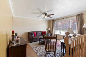 Living area with light wood-type flooring, a textured ceiling, ornamental molding, and ceiling fan