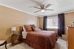 Bedroom with ornamental molding, a textured ceiling, ceiling fan, and light carpet