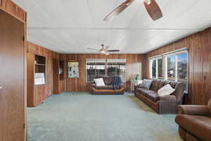Living room with wooden walls, light carpet, a ceiling fan, and a textured ceiling
