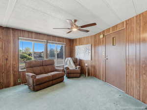 Living area featuring carpet flooring, ceiling fan, and wooden walls