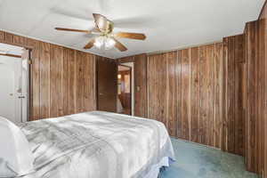 Carpeted bedroom featuring ceiling fan, a closet, and wood walls