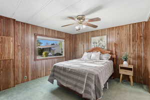 Carpeted bedroom featuring ceiling fan, wood walls, and a textured ceiling