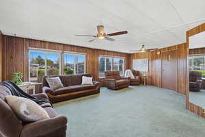 Living room with carpet flooring, wooden walls, and ceiling fan