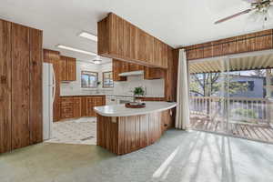 Kitchen featuring light countertops, wood finish cabinetry, wood walls, white appliances, and ceiling fan