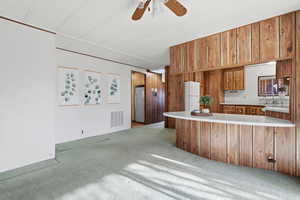 Kitchen with wood finish cabinetry, light countertops, light carpet, a peninsula, and ceiling fan